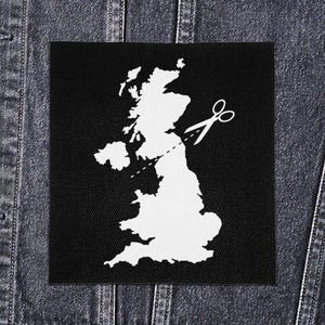 May include: A black patch showing a white outline of the British Isles with scissors cutting across the map. The patch is set against a denim jacket.