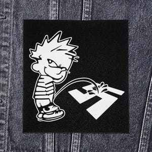 May include: Black square patch with a cartoon boy urinating on a white swastika symbol. The boy wears a striped top and trainers. The patch is set against a denim background.