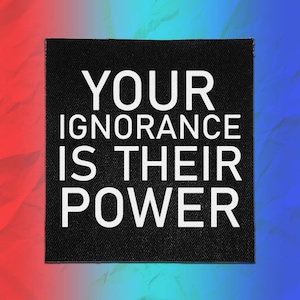 May include: A square black fabric patch featuring the white text YOUR IGNORANCE IS THEIR POWER in a bold, sans-serif font. The patch has a visible woven texture and clean, straight edges, presented against a vibrant red and blue gradient background.