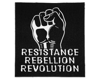 May include: A square black fabric patch featuring a white graphic illustration of a raised fist. Below the fist, the text RESISTANCE REBELLION REVOLUTION is printed in a bold, white, sans-serif font. The patch has a visible woven texture.