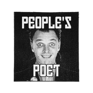 Pode incluir: Um emblema de tecido quadrado em preto e branco com um retrato em meio-tom de uma pessoa com um sorriso largo. O texto "PEOPLE'S" está impresso em letras brancas acima do retrato e a palavra "POET" está em letras brancas abaixo.