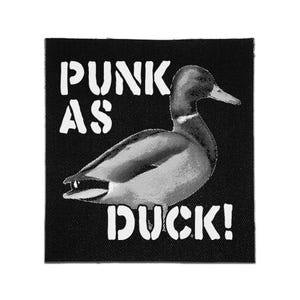 May include: A square black fabric patch featuring a white halftone illustration of a duck in the center. The text PUNK AS DUCK! is printed in a bold, distressed white font, with PUNK AS positioned above the duck and DUCK! below it.