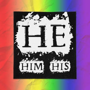 May include: A square fabric patch with a black background and a white distressed ink-style graphic. The text HE is printed in large letters at the top, with the words HIM and HIS printed in smaller letters below, all in a serif font style.