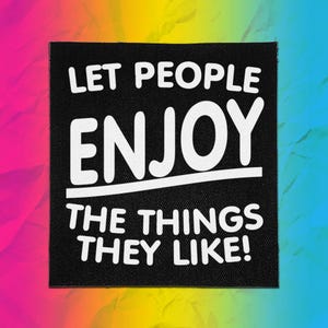 Puede incluir: Un parche de tela cuadrado de color negro con el texto en blanco LET PEOPLE ENJOY THE THINGS THEY LIKE! en una fuente negrita sin remates. El diseño incluye una línea horizontal blanca que separa la palabra ENJOY del resto del texto.