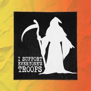May include: A square black fabric patch featuring a white silhouette of a hooded figure holding a scythe. The text "I SUPPORT EVERYONE'S TROOPS" is printed in white capital letters on the lower left side of the patch against the black background.