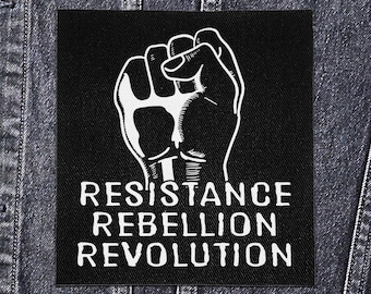 May include: Black square patch with a white raised fist graphic and the words "RESISTANCE REBELLION REVOLUTION" in white block letters. The patch is set against a denim jacket.