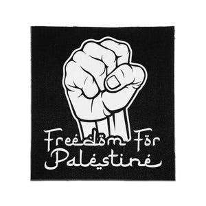 Pode incluir: Um emblema quadrado de tecido preto com uma ilustração gráfica branca de um punho levantado. Abaixo do punho, o texto "Freedom För Palestine" está impresso numa fonte branca estilizada. O design está centrado no fundo preto.