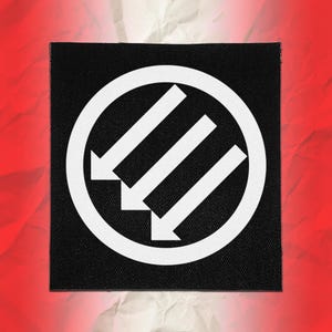 Może przedstawiać: Kwadratowa czarna naszywka z tkaniny z białą okrągłą obwódką, wewnątrz której znajdują się trzy równoległe białe strzałki skierowane ukośnie w lewo w dół. Wzór jest wyśrodkowany na czarnym tle, tworząc kontrastujący emblemat graficzny.