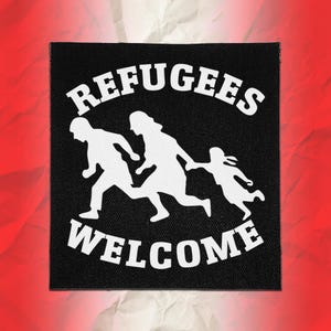May include: A square black fabric patch featuring a white graphic of three figures running, with the text REFUGEES arched above and WELCOME arched below in a bold, white, sans-serif font. The design is centred on a textured black background.