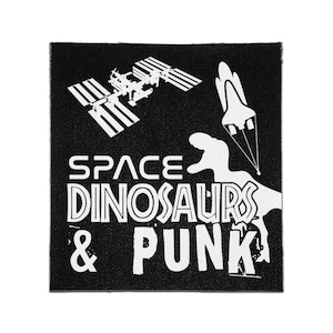 May include: A square black fabric patch featuring a white graphic print. The design includes a space station, a space shuttle, and a dinosaur silhouette. The text reads SPACE DINOSAURS & PUNK in a bold, stylised white font across the lower section.