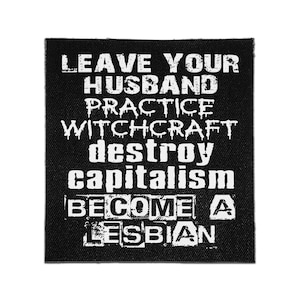 May include: A square black fabric patch featuring white distressed-style text that reads: LEAVE YOUR HUSBAND, PRACTICE WITCHCRAFT, DESTROY CAPITALISM, BECOME A LESBIAN. The lettering has a rough, textured appearance against the dark background.