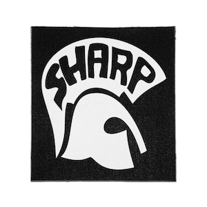 May include: A square fabric patch featuring a black background with a white graphic design. The design depicts a stylized helmet shape with the word SHARP integrated into the upper curved section of the helmet in bold, black capital letters.