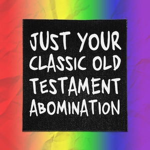 May include: A square black fabric patch featuring the white text "JUST YOUR CLASSIC OLD TESTAMENT ABOMINATION" printed in a bold, sans-serif font. The patch has a visible woven texture and is set against a vibrant, multi-colored rainbow background.