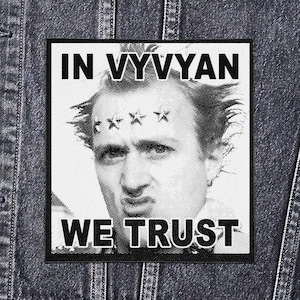 May include: Square black and white patch featuring a halftone portrait of a man with stars above his eyes, and the text "IN VYYVYAN WE TRUST". The patch is set against a denim jacket.