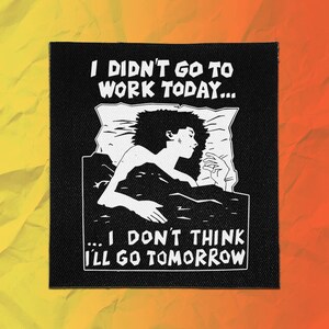 May include: A square black fabric patch featuring a white screen-printed illustration of a person sleeping in bed. The text reads I DIDN'T GO TO WORK TODAY... and ...I DON'T THINK I'LL GO TOMORROW in a bold, blocky white font above and below the figure.