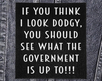 May include: A black square patch with white text that reads: "IF YOU THINK I LOOK DODGY, YOU SHOULD SEE WHAT THE GOVERNMENT IS UP TO!!!" The patch is sewn onto a denim jacket.