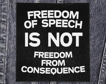 May include: Black square patch with white text that reads "FREEDOM OF SPEECH IS NOT FREEDOM FROM CONSEQUENCE." The patch is sewn onto a dark denim jacket. The text is in a bold, sans-serif font.