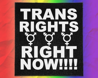 May include: A square black fabric patch featuring the white text TRANS RIGHTS RIGHT NOW!!!! arranged in three lines. Between the second and third lines of text, there are three white gender symbols, each featuring a cross, an arrow, and a loop.