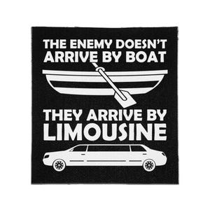 May include: A square black fabric patch featuring white screen-printed graphics and text. The design includes a rowboat with an oar and a limousine, accompanied by the text: THE ENEMY DOESN'T ARRIVE BY BOAT THEY ARRIVE BY LIMOUSINE.