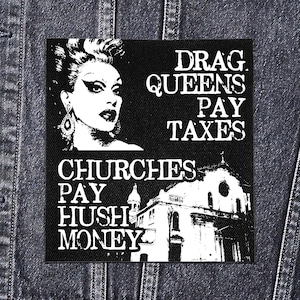 Puede incluir: Parche en blanco y negro con una ilustración de drag queen y el texto "DRAG QUEENS PAY TAXES" y "CHURCHES PAY HUSH MONEY". El parche es rectangular y parece ser de tela.