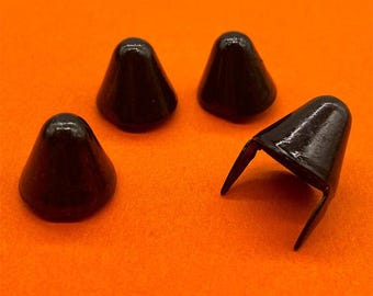 May include: Four black metal cone-shaped studs with a smooth, glossy finish. Three of the studs are positioned upright, while one stud is lying on its side, revealing two sharp prongs extending from the base for attachment to fabric or leather.