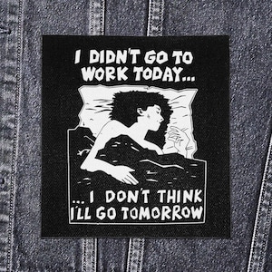 Peut inclure: Écusson noir et blanc avec le texte "I DIDN'T GO TO WORK TODAY... ...I DON'T THINK I'LL GO TOMORROW". L'écusson représente une personne au lit, avec des cheveux bouclés, dormant sur un oreiller.