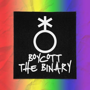Pode incluir: Um emblema quadrado de tecido preto com um símbolo circular branco com uma cruz e uma forma de asterisco no topo. Abaixo do símbolo, o texto BOYCOTT THE BINARY está impresso numa fonte branca de estilo manuscrito e textura tecida.