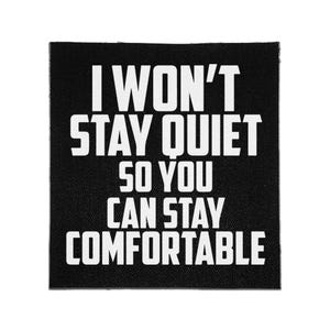 Op de afbeelding: Een vierkante zwarte stoffen patch met de witte tekst I WON'T STAY QUIET SO YOU CAN STAY COMFORTABLE in een vet, schreefloos lettertype. De patch heeft een zichtbare geweven textuur en strakke randen, ontworpen om op kleding of accessoires te bevestigen.
