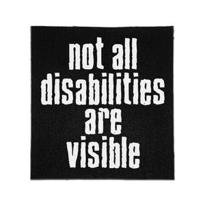 以下が含まれることがあります： 黒い正方形の布製パッチ。太字のサンセリフ体で「not all disabilities are visible」という白い文字がプリントされている。文字は少し掠れたような質感で、無地の黒い背景に配置されている。