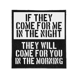Puede incluir: Un parche de tela cuadrado con un diseño en blanco y negro. La mitad superior presenta texto negro sobre fondo blanco que dice IF THEY COME FOR ME IN THE NIGHT. La mitad inferior presenta texto blanco sobre fondo negro que dice THEY WILL COME FOR YOU IN THE MORNING.