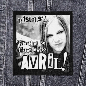 May include: Black and white patch featuring a portrait of Avril Lavigne with the text "pistols? I'd rather be listening to AVRIL!". The patch is rectangular with a black border and is likely made of fabric.
