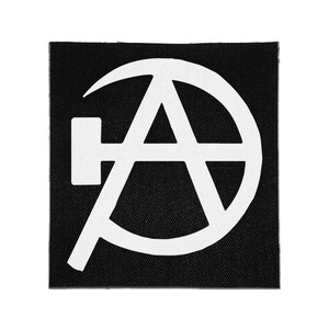 Op de afbeelding: Een vierkante zwarte stoffen patch met een wit grafisch ontwerp. Het ontwerp bestaat uit een hoofdletter A omsloten door een cirkelvorm, met een horizontaal hamericoon dat vanaf de linkerkant van de letter A in de cirkel uitsteekt.