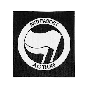 May include: A square black fabric patch featuring a white circular emblem. Inside the circle is a graphic of two overlapping flags and the text ANTI FASCIST ACTION in a distressed, stencil-style font. The design is centered on the black background.