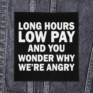 May include: Black square patch with white text that reads: "LONG HOURS LOW PAY AND YOU WONDER WHY WE'RE ANGRY." The patch is on a denim jacket.