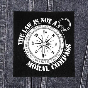 May include: Black square patch with a white compass design and the text "THE LAW IS NOT A MORAL COMPASS" in a circular layout. The compass features directional markings and degree indicators.