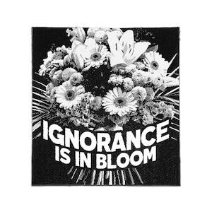 May include: A square black and white fabric patch featuring a halftone graphic of a floral bouquet. The text "IGNORANCE IS IN BLOOM" is printed in bold white capital letters across the bottom portion of the design, centered below the flowers.