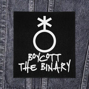 Op de afbeelding: Zwart vierkantige patch met een wit genderqueer symbool en de tekst "BOYCOTT THE BINARY" in een handgeschreven lettertype. De patch is geplaatst op een donkere denim achtergrond.