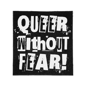 May include: A square fabric patch with a black background and white distressed lettering that reads QUEER WITHOUT FEAR! The text is arranged in three lines with a bold, blocky font style that features a weathered, textured appearance throughout.
