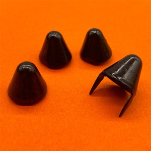May include: Four black metal cone-shaped furniture feet with a square base. The feet are on an orange surface.