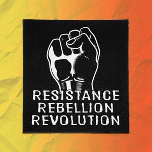 May include: A square black fabric patch featuring a white graphic illustration of a raised fist. Below the fist, the text RESISTANCE REBELLION REVOLUTION is printed in a bold, white, sans-serif font, centered on the black background.