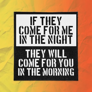 May include: A square fabric patch featuring a two-tone design. The top half is white with black stencil-style text reading IF THEY COME FOR ME IN THE NIGHT. The bottom half is black with white stencil-style text reading THEY WILL COME FOR YOU IN THE MORNING.