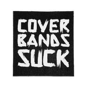 May include: A square black fabric patch featuring the white text COVER BANDS SUCK in a distressed, brush-stroke style font. The lettering is arranged in three stacked lines, creating a high-contrast graphic design on the woven textile surface.