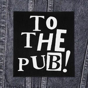 May include: A black square patch with the text "TO THE PUB!" in white, bold, uppercase letters. The patch is attached to a denim jacket.