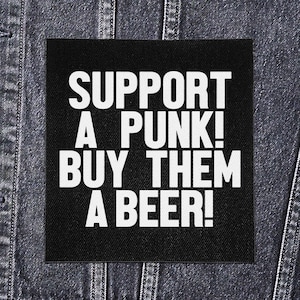 Może przedstawiać: Czarna kwadratowa naszywka z białym napisem: "SUPPORT A PUNK! BUY THEM A BEER!" na ciemnej kurtce dżinsowej. Modny dodatek.