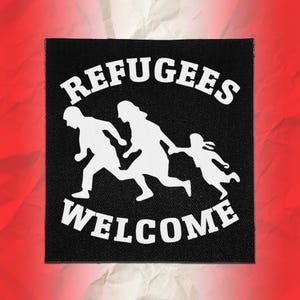 May include: A square black fabric patch featuring a white graphic of three figures running together. The text REFUGEES is printed in a white arched font above the figures, and the word WELCOME is printed in a white font below the figures.