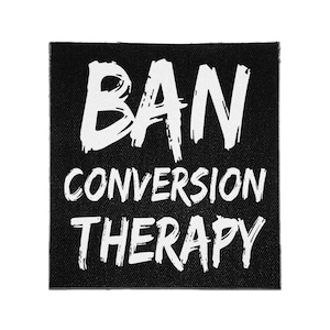 Puede incluir: Un parche de tela cuadrado de color negro con el texto en blanco BAN CONVERSION THERAPY en un estilo de letra manuscrita, audaz y desgastado. Las letras están dispuestas en tres líneas, con la palabra BAN en un tamaño mayor arriba.