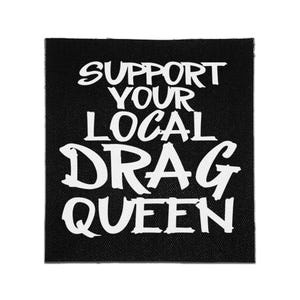 May include: A square black fabric patch featuring the white text SUPPORT YOUR LOCAL DRAG QUEEN in a bold, distressed, brush-stroke style font. The design is centered on the patch, which has a visible woven texture throughout the black background.