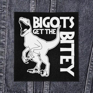 May include: Black square patch with white text and a dinosaur illustration. The text reads "BIGOTS GET THE BITEY". The dinosaur is a raptor with its mouth open, and the patch is on a denim jacket.