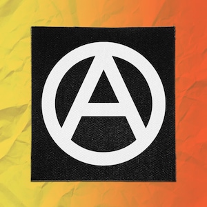 May include: A square-shaped patch featuring a black background with a large, white, centered letter A enclosed within a white circle. The design is a classic anarchist symbol, presented as a flat, embroidered-style textile patch with clean, bold lines.