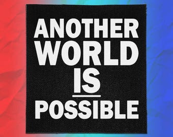 May include: A square black fabric patch featuring the white text "ANOTHER WORLD IS POSSIBLE" in a bold, sans-serif font. The text is arranged in four lines with a horizontal line separating the words "IS" and "POSSIBLE" on the patch surface.